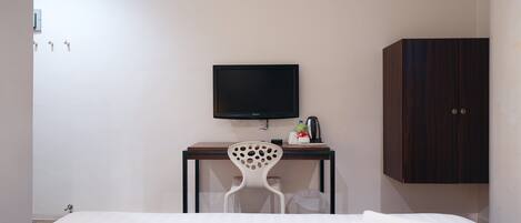 A hotel room with a bed, a desk with a TV, a chair, and a wardrobe.