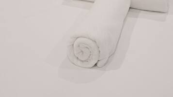 A neatly made bed with white linens and a rolled towel.