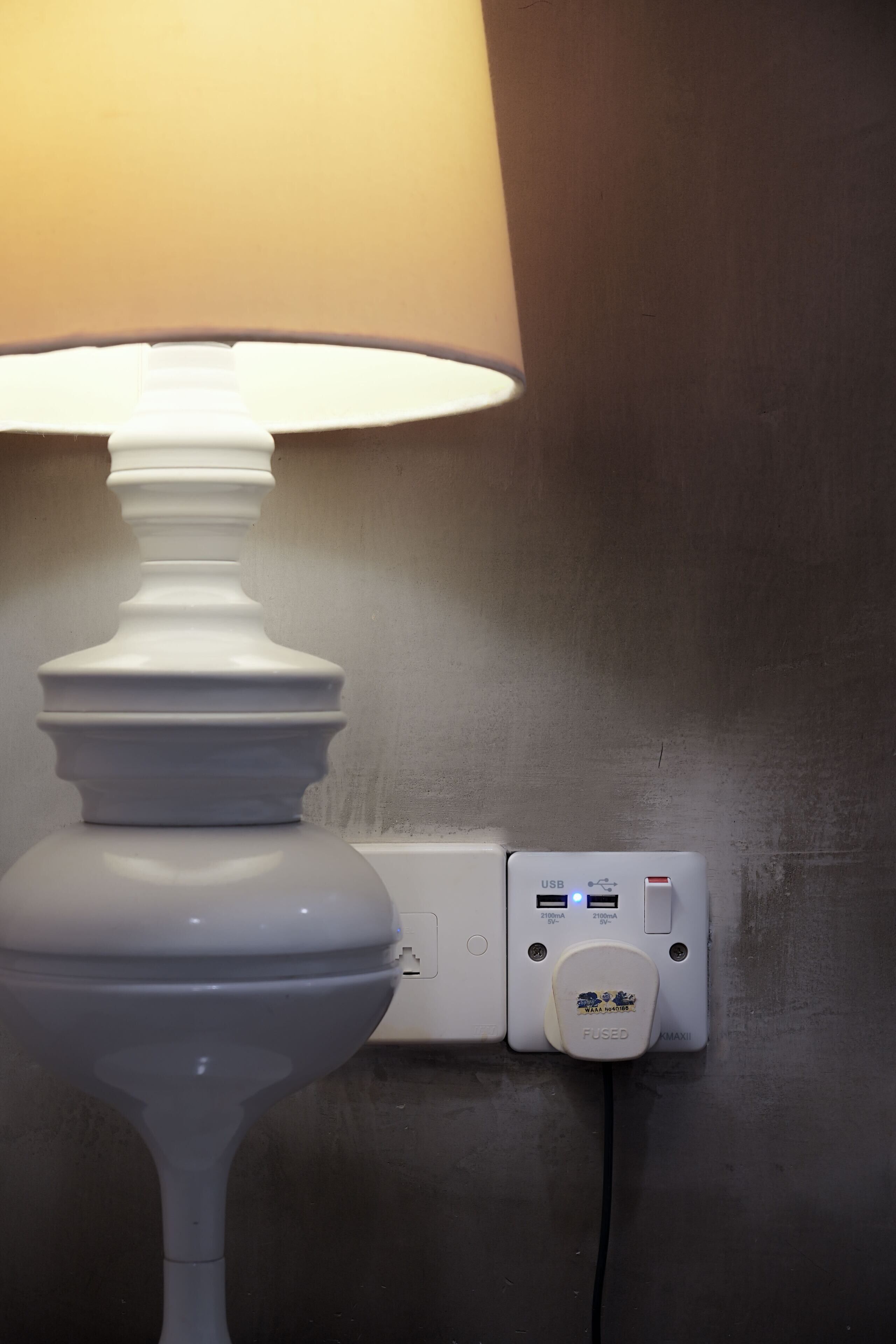 A white lamp with a beige shade and a USB charging port on a wall.