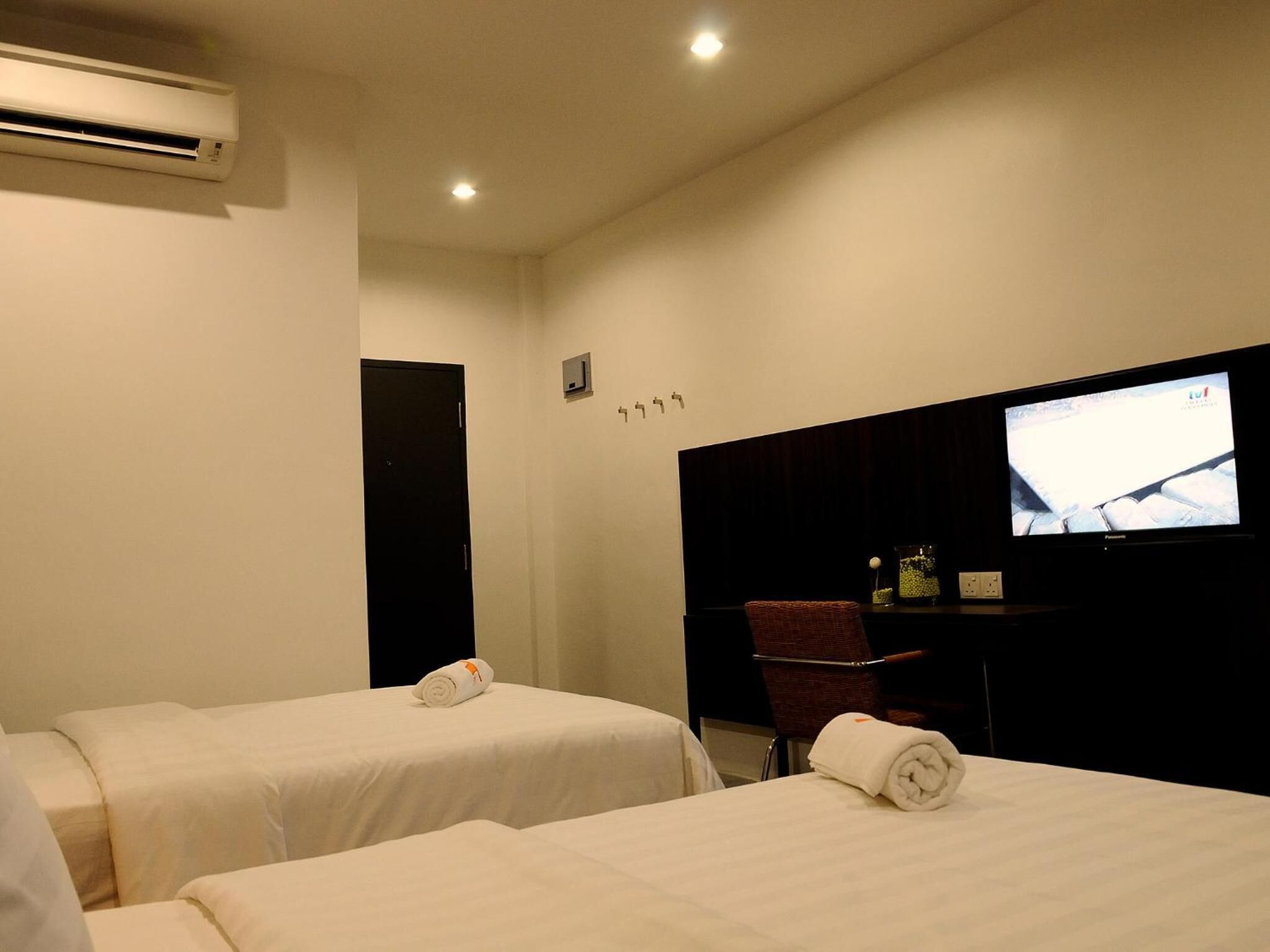 A hotel room with two beds, a TV, a desk, and an air conditioner.
