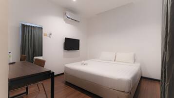 Una habitación de hotel con cama, televisión montada en la pared, una mesa con sillas y un equipo de aire acondicionado.