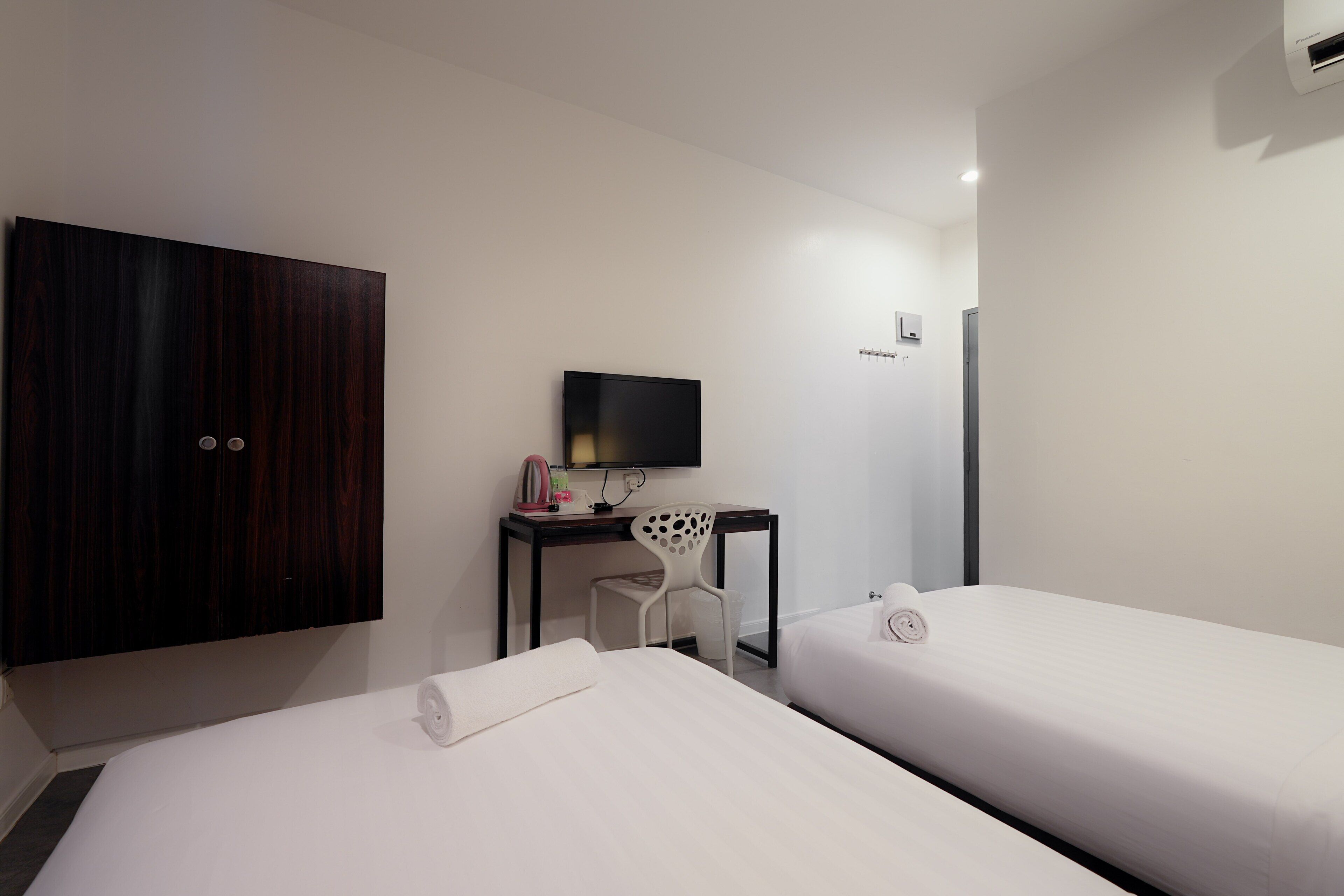 Ett hotellrum med två separata sängar, ett skrivbord med en stol, en TV och en garderob.