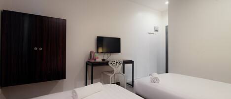 A hotel room with two single beds, a desk with a chair, a TV, and a wardrobe.