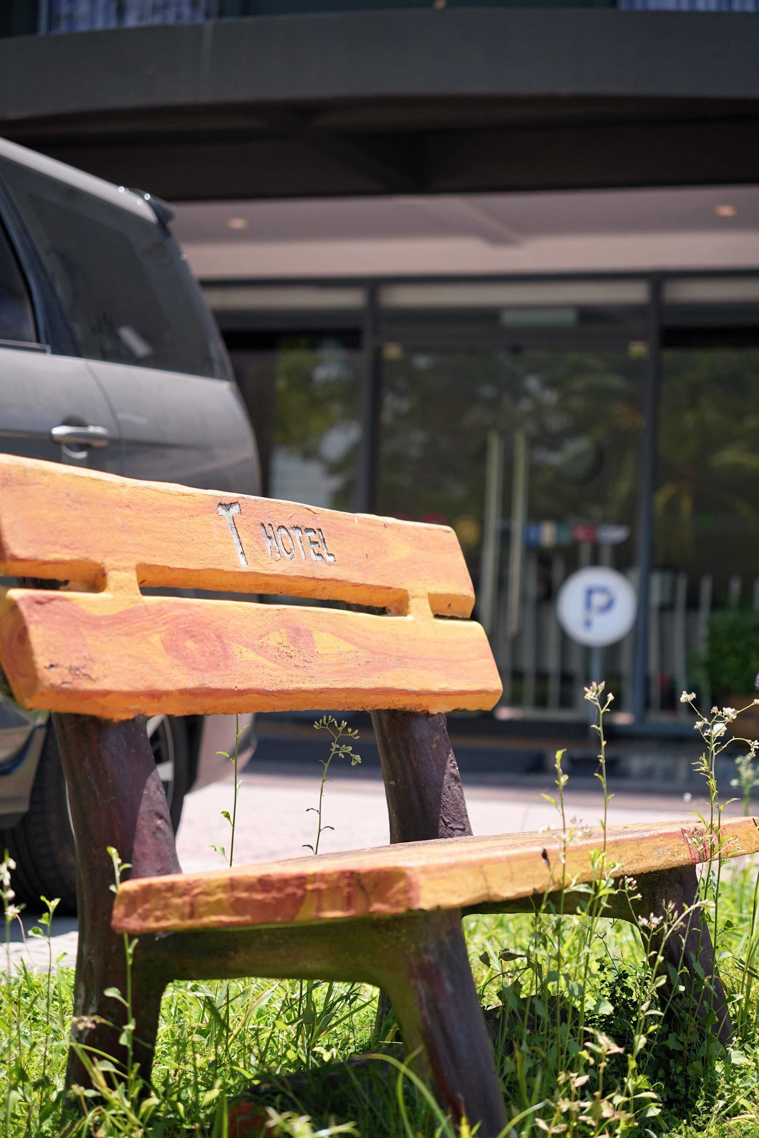 A wooden bench with "HOTEL" engraved on it, placed in front of a building with a parking sign.