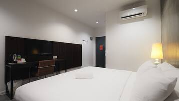 A hotel room with a bed, a desk with a chair, a television, and an air conditioning unit.