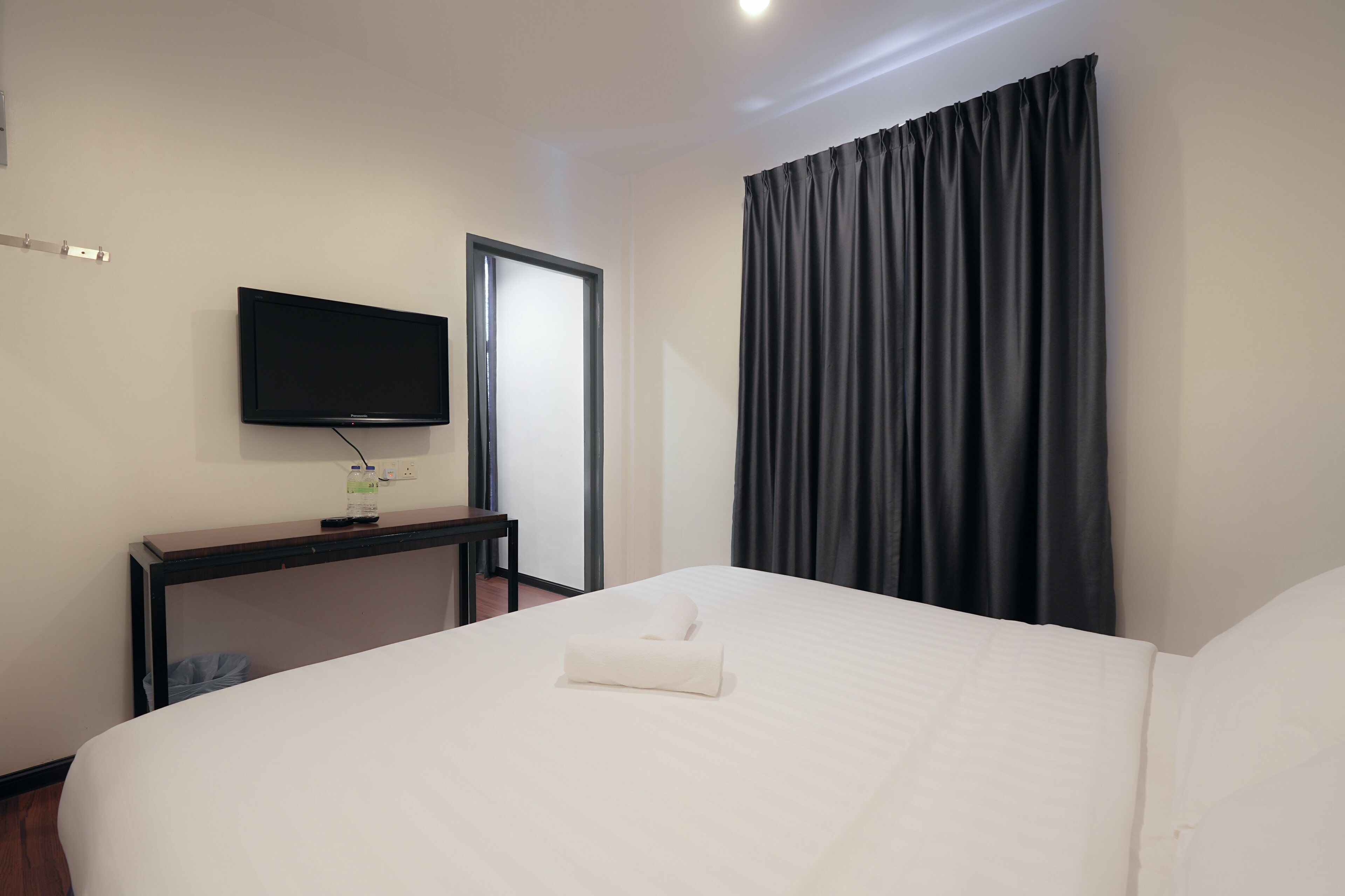 Une chambre d’hôtel avec un lit, un téléviseur fixé au mur, un bureau et une fenêtre avec des rideaux.