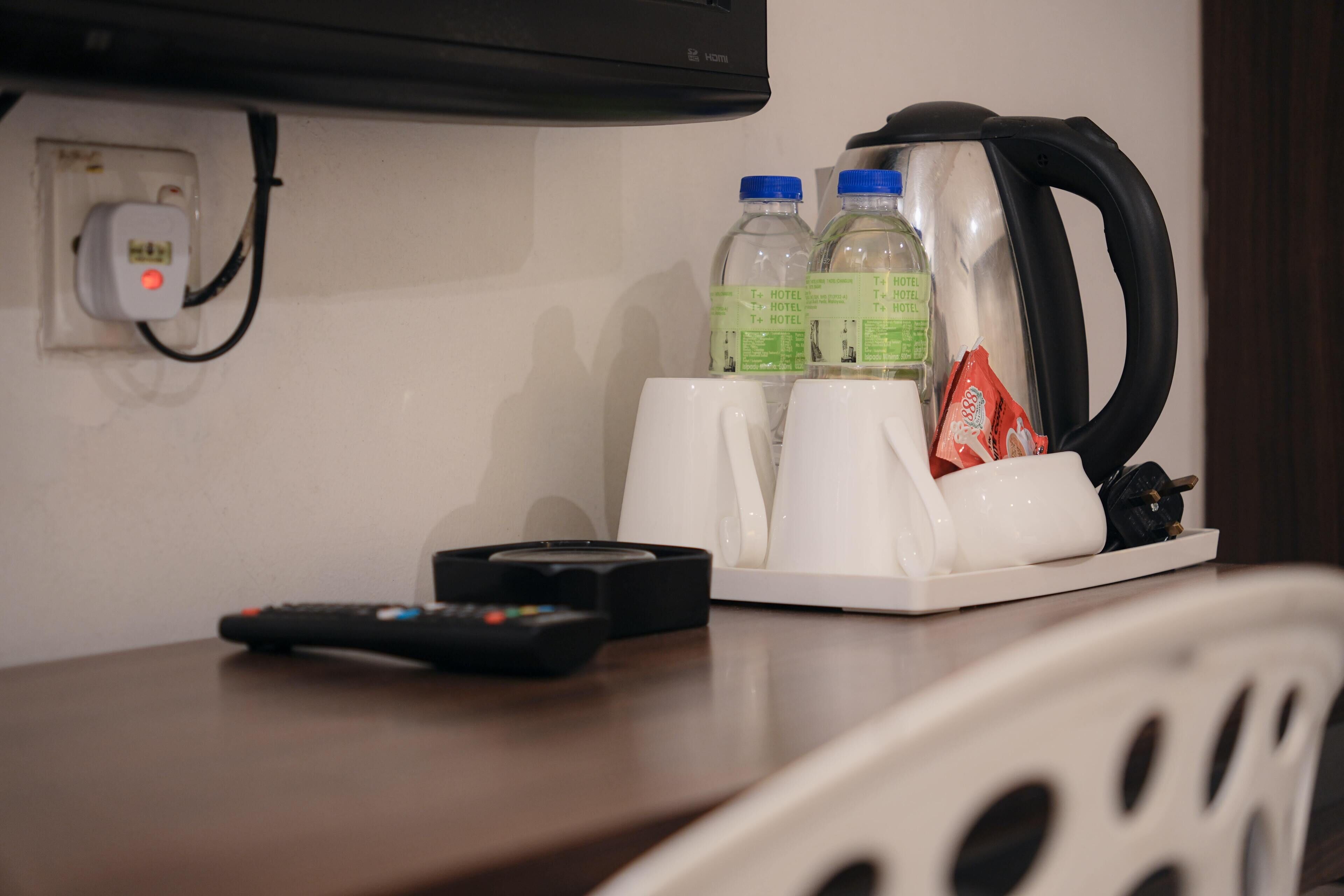Une chambre d’hôtel équipée d’une télévision, d’une télécommande, d’une bouilloire et de deux bouteilles d’eau posées sur la table.