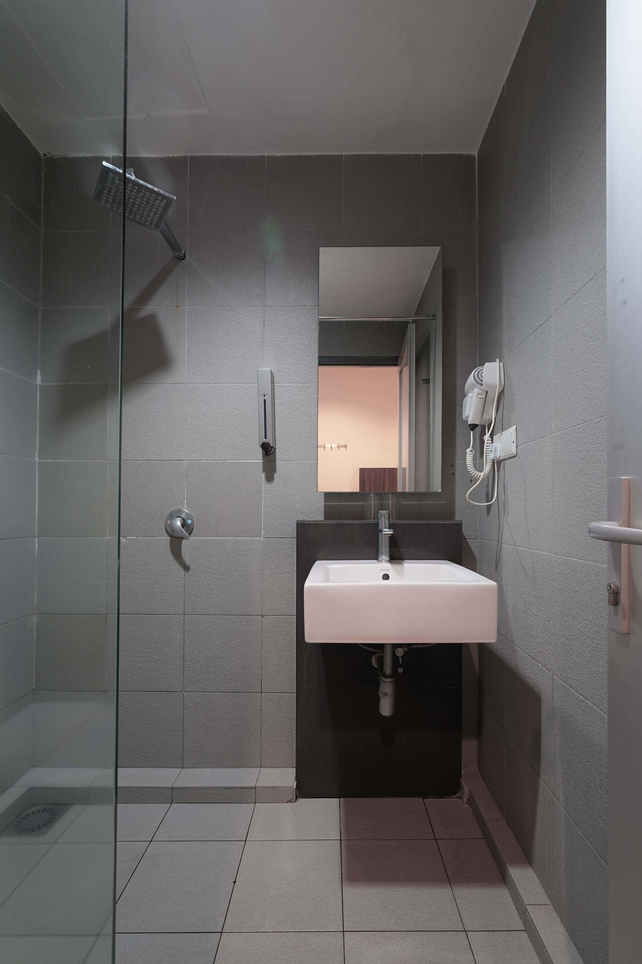 A modern bathroom with a glass shower enclosure, a white sink, and a hairdryer mounted on the wall.