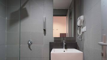 A modern bathroom with a glass shower enclosure, a white sink, and a hairdryer mounted on the wall.