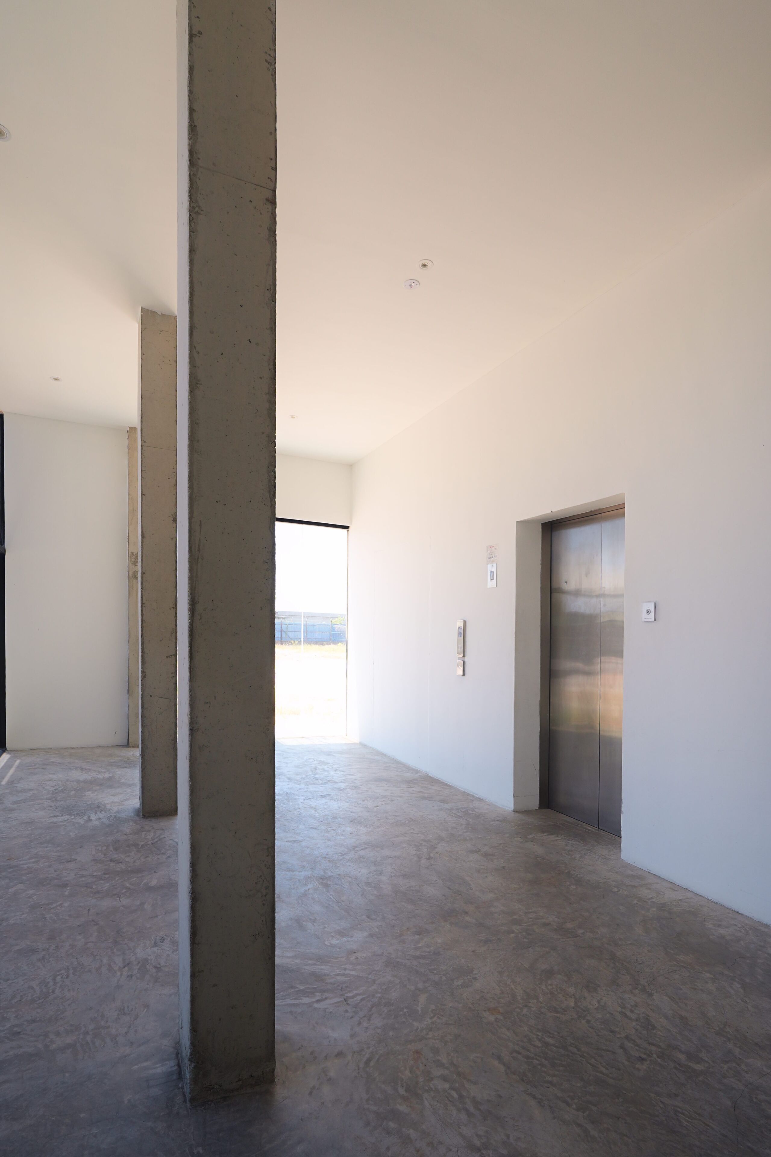 A spacious, modern interior with concrete pillars, a large window, and an elevator.