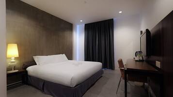 Une chambre d’hôtel avec un lit, un bureau, une chaise, une lampe et un grand miroir.