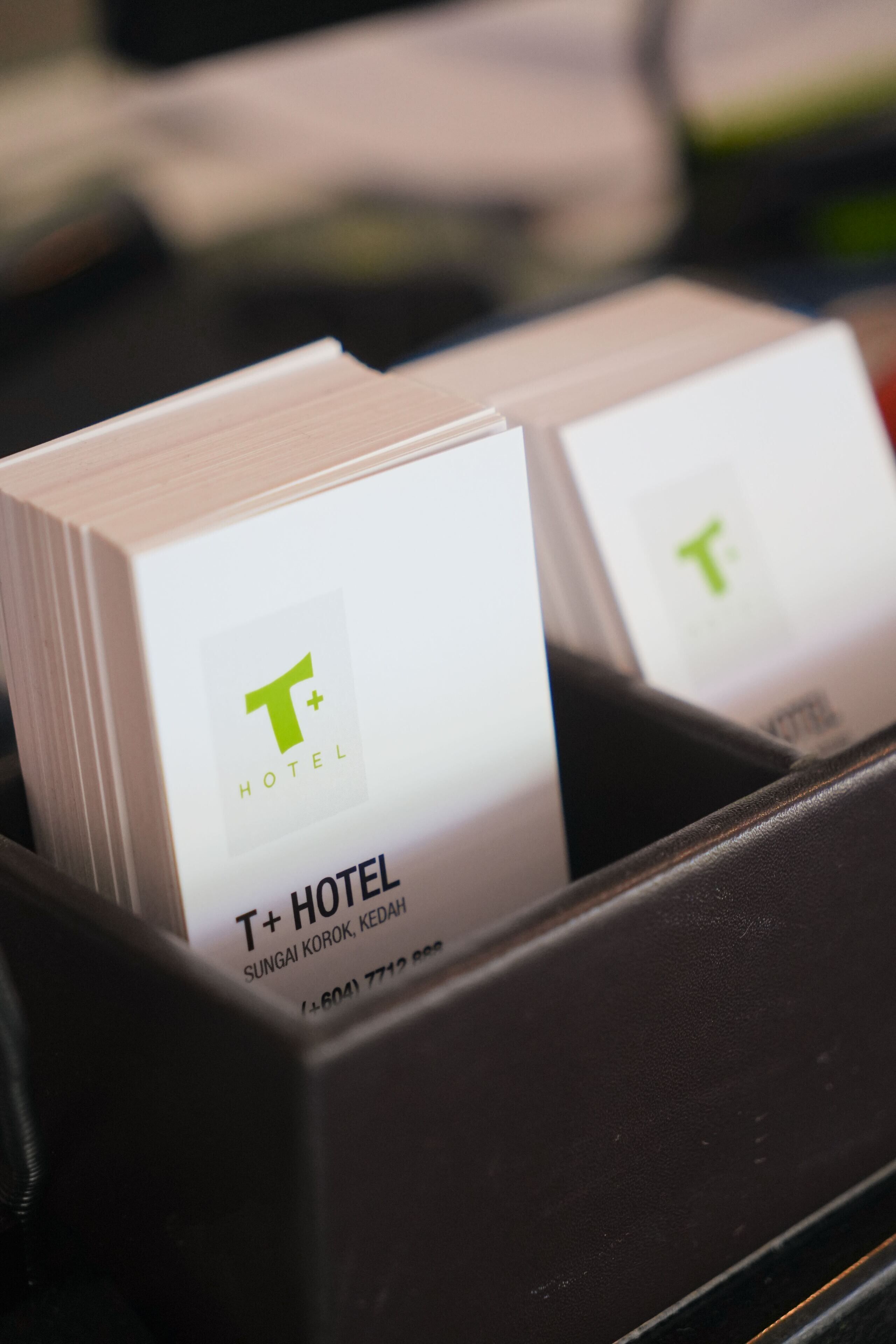 Soporte negro para tarjetas de hotel con dos tarjetas de presentación de T+ HOTEL, que incluyen la dirección y el número de teléfono.