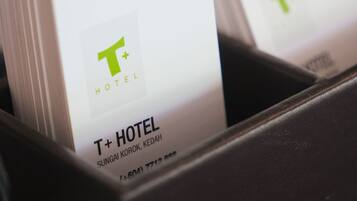 Soporte negro para tarjetas de hotel con dos tarjetas de presentación de T+ HOTEL, que incluyen la dirección y el número de teléfono.