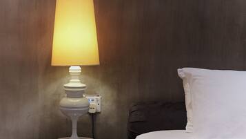 A bed with white bedding, a bedside table with a white lamp, and a dark-colored wall.