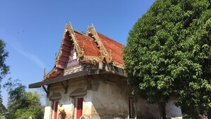 A traditional building with a red tiled roof and ornate decorations, surrounded by greenery and stone structures. - Q Zone Boutique (Ayutthaya)