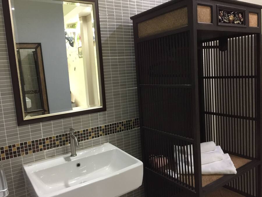 Un baño con un lavamanos blanco, un espejo y un mueble de madera oscura con un estante tejido.