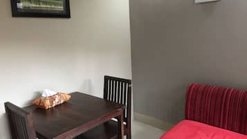 Un comedor con una mesa y sillas de madera, un sofá rojo y dos cuadros enmarcados en las paredes.