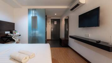 Quarto de hotel moderno com uma cama, uma televisão presa à parede, uma escrivaninha com uma cadeira e um banheiro visível através de uma porta de vidro.