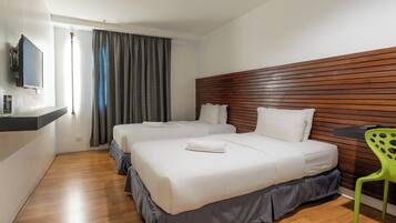 A hotel room with two beds, a wooden headboard, a TV mounted on the wall, and a green chair.