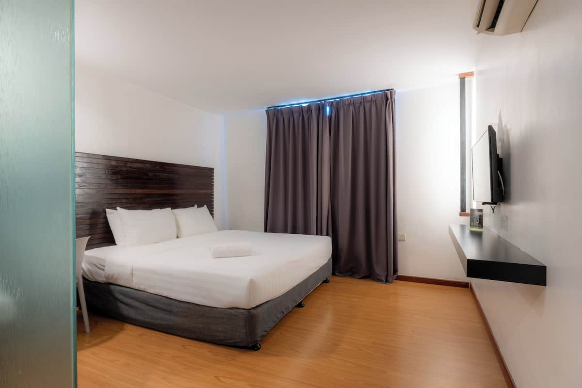 Moderni hotellihuone, jossa on suuri sänky, seinälle asennettu taulutelevisio ja puulattia.