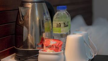 A tray with a stainless steel kettle, a bottle of water, a packet of white coffee, and two white mugs.