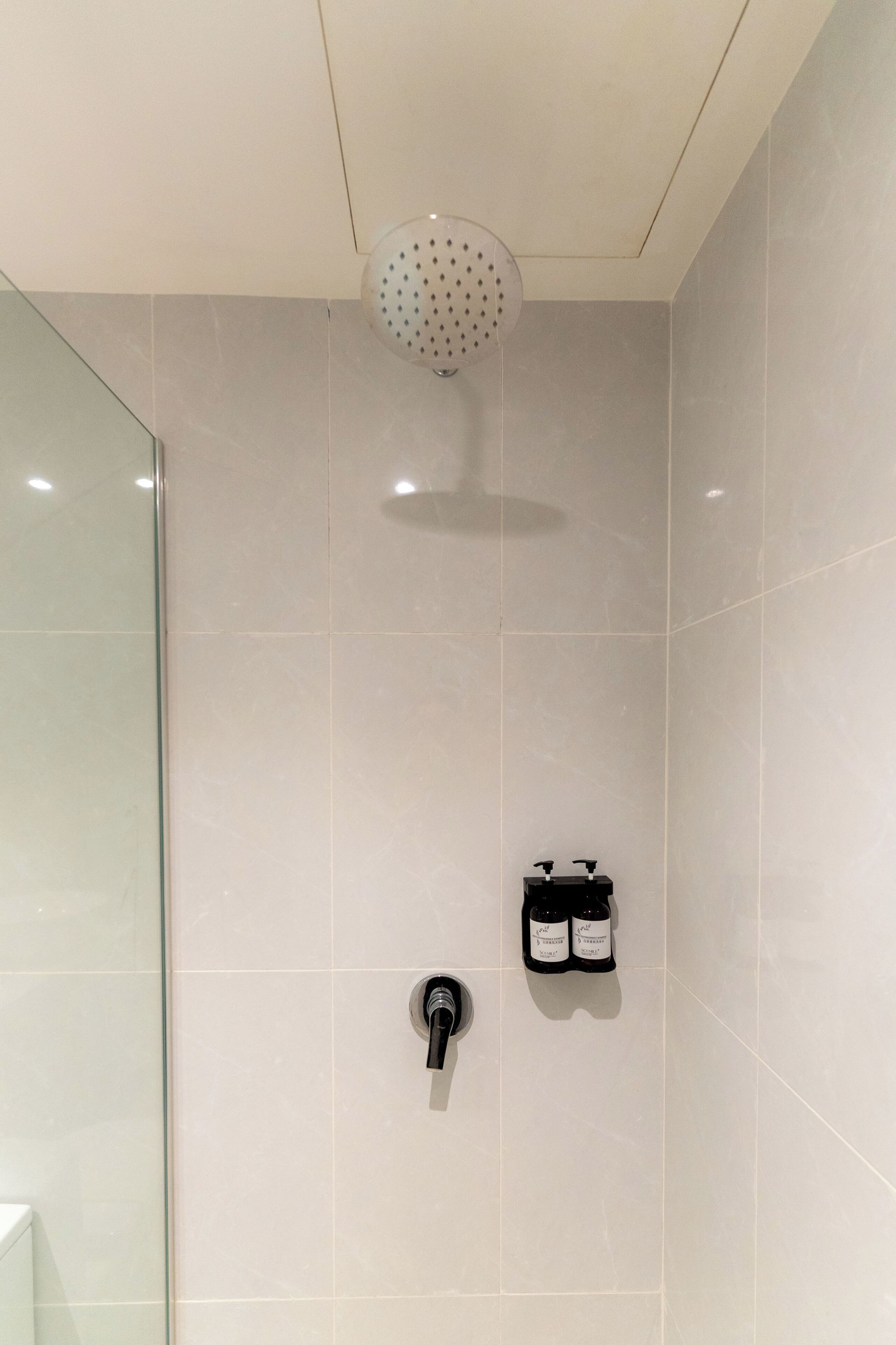 A modern bathroom with a glass shower enclosure, a wall-mounted faucet, and two bottles of shampoo.