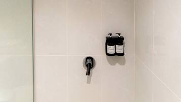 A modern bathroom with a glass shower enclosure, a wall-mounted faucet, and two bottles of shampoo.