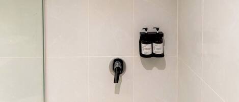 A modern bathroom with a glass shower enclosure, a wall-mounted faucet, and two bottles of shampoo.