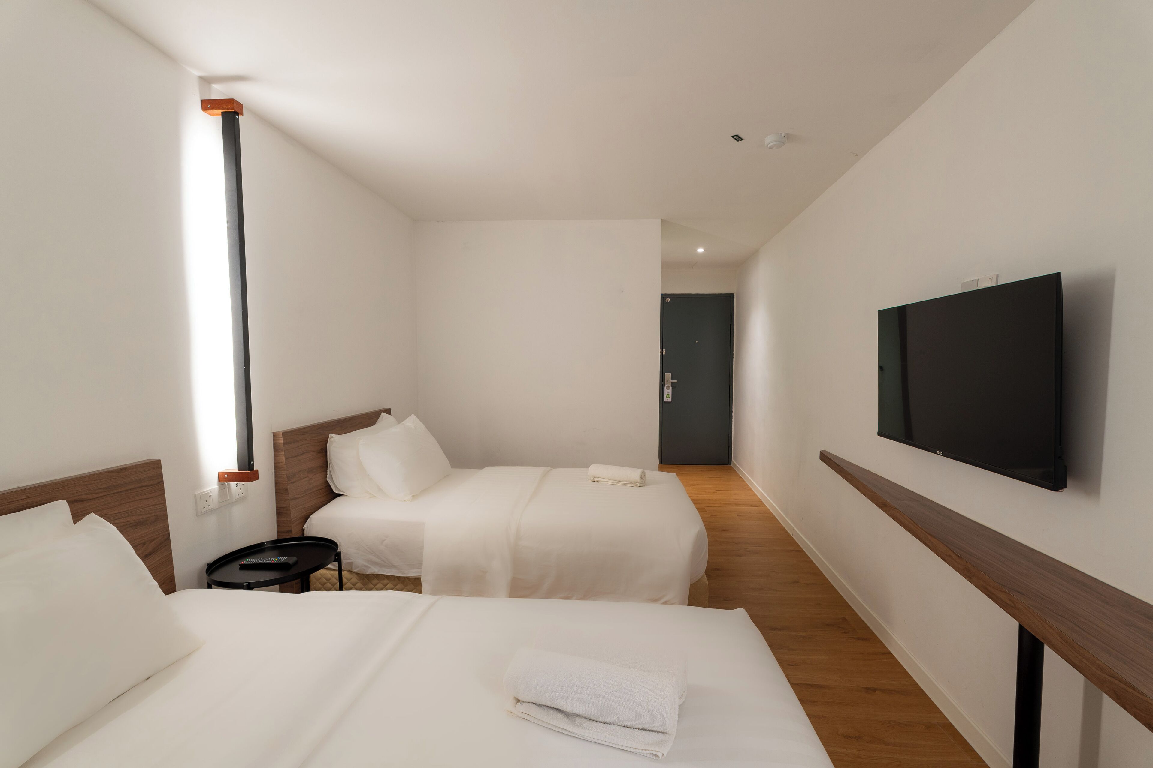 A hotel room with two beds, a TV mounted on the wall, and a wooden floor.