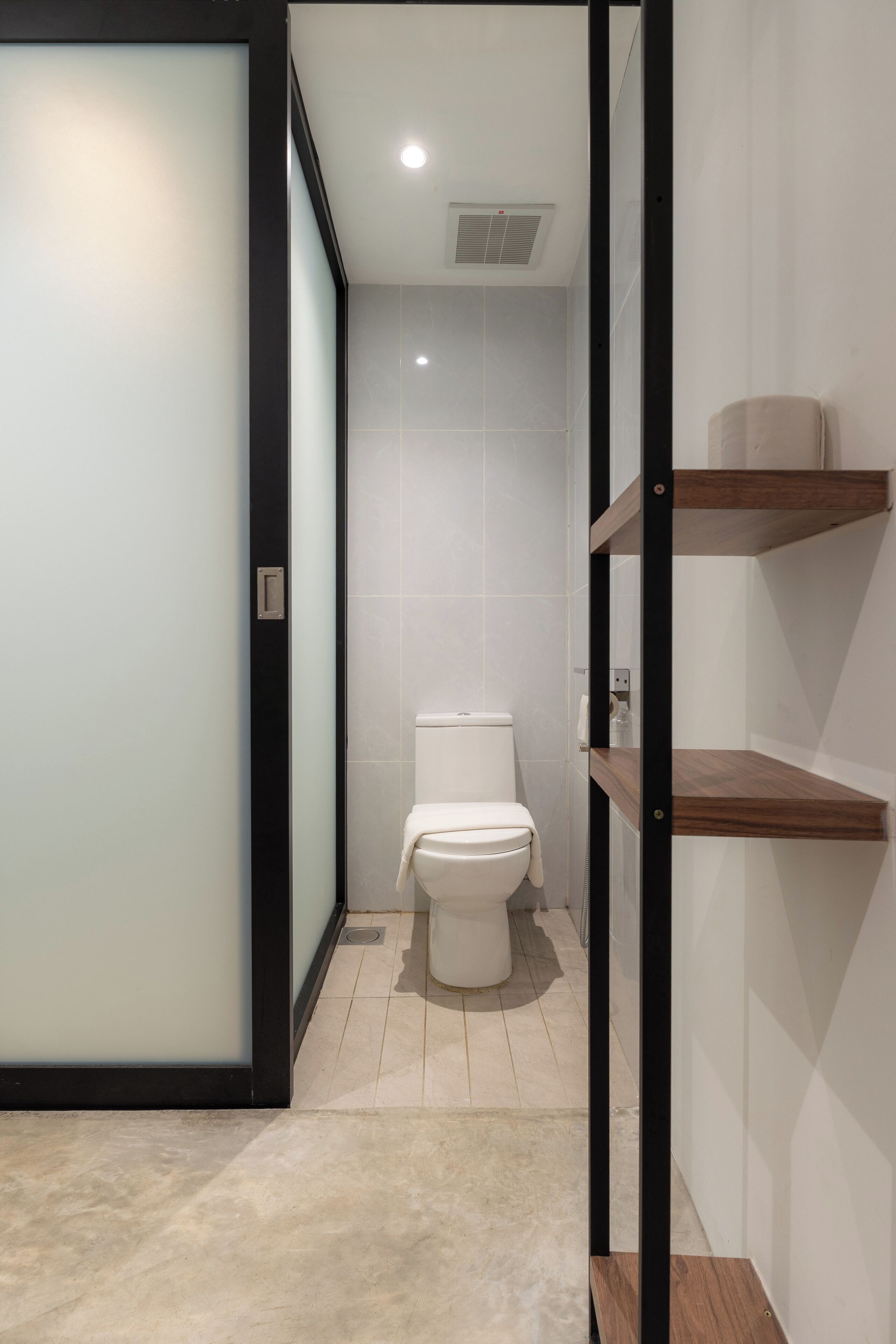 A modern bathroom with a toilet, a shower area, and a vanity with shelves.