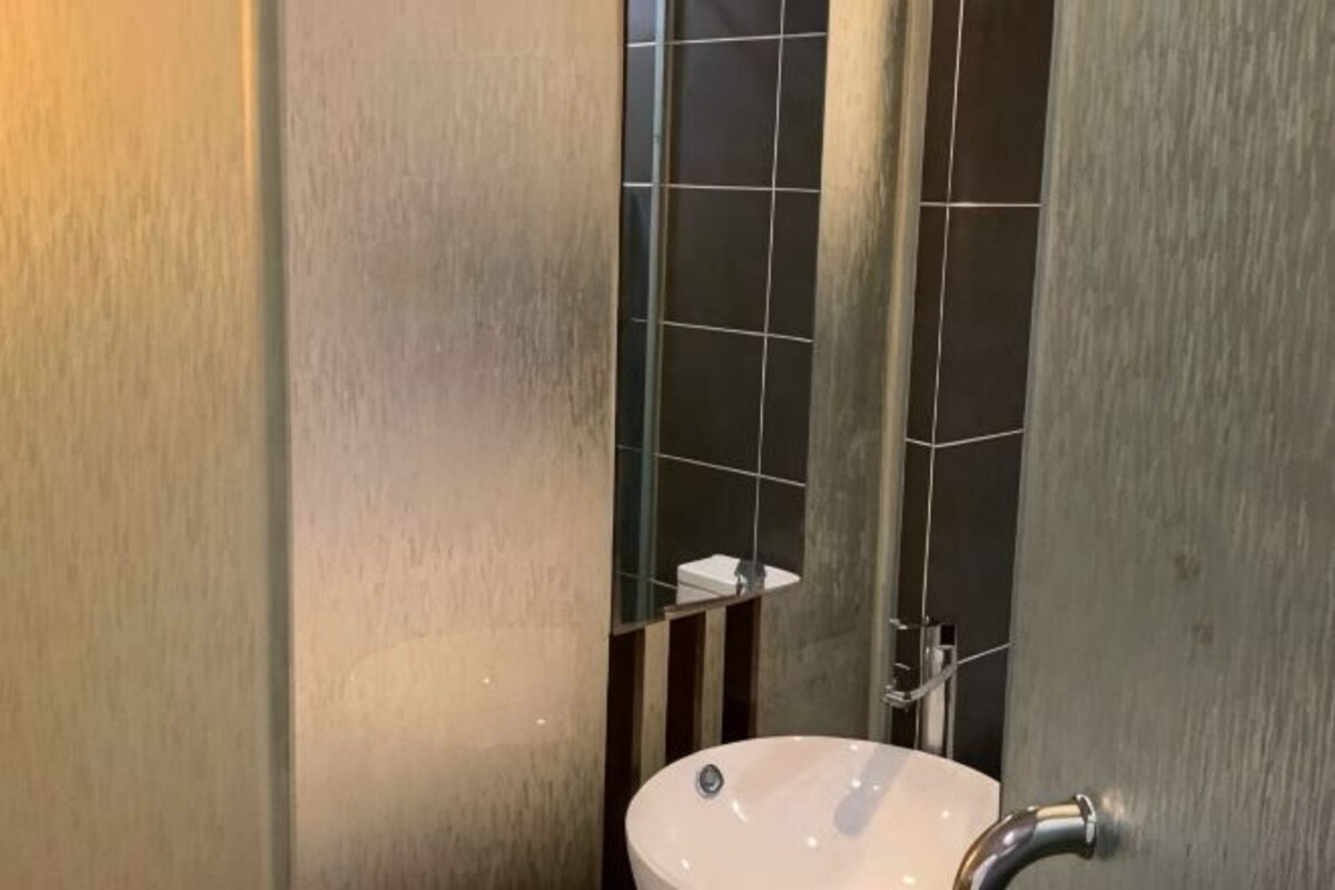 A bathroom with a white sink, a mirror, and dark tiled walls.