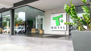 A modern hotel entrance with a glass facade, a large T+ sign, and a potted plant in the foreground. - T+ Hotel Sungai Petani (Sungai Petani)