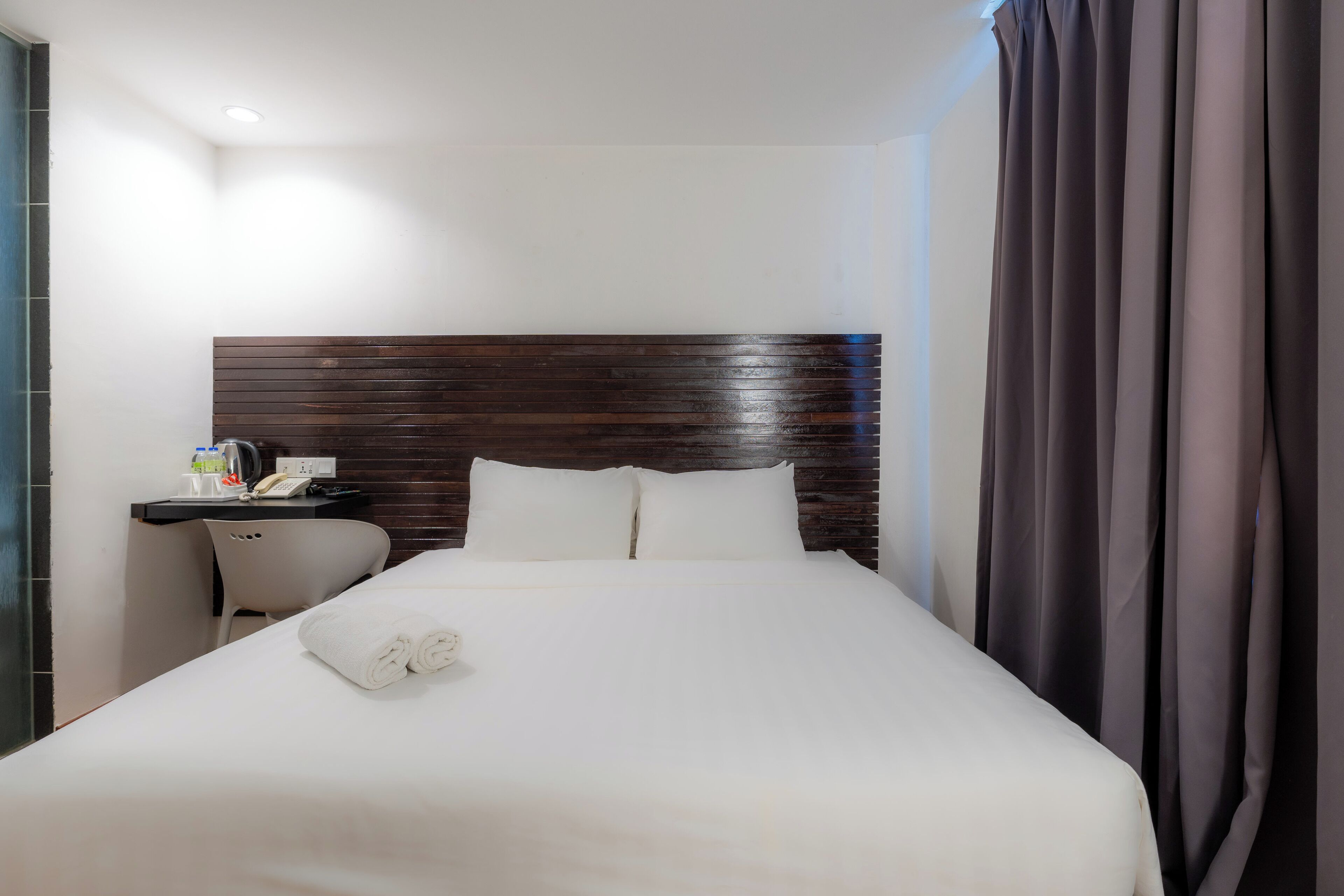 Hotelkamer met een groot bed, een houten hoofdbord, een bureau met telefoon en lamp, en een stoel.