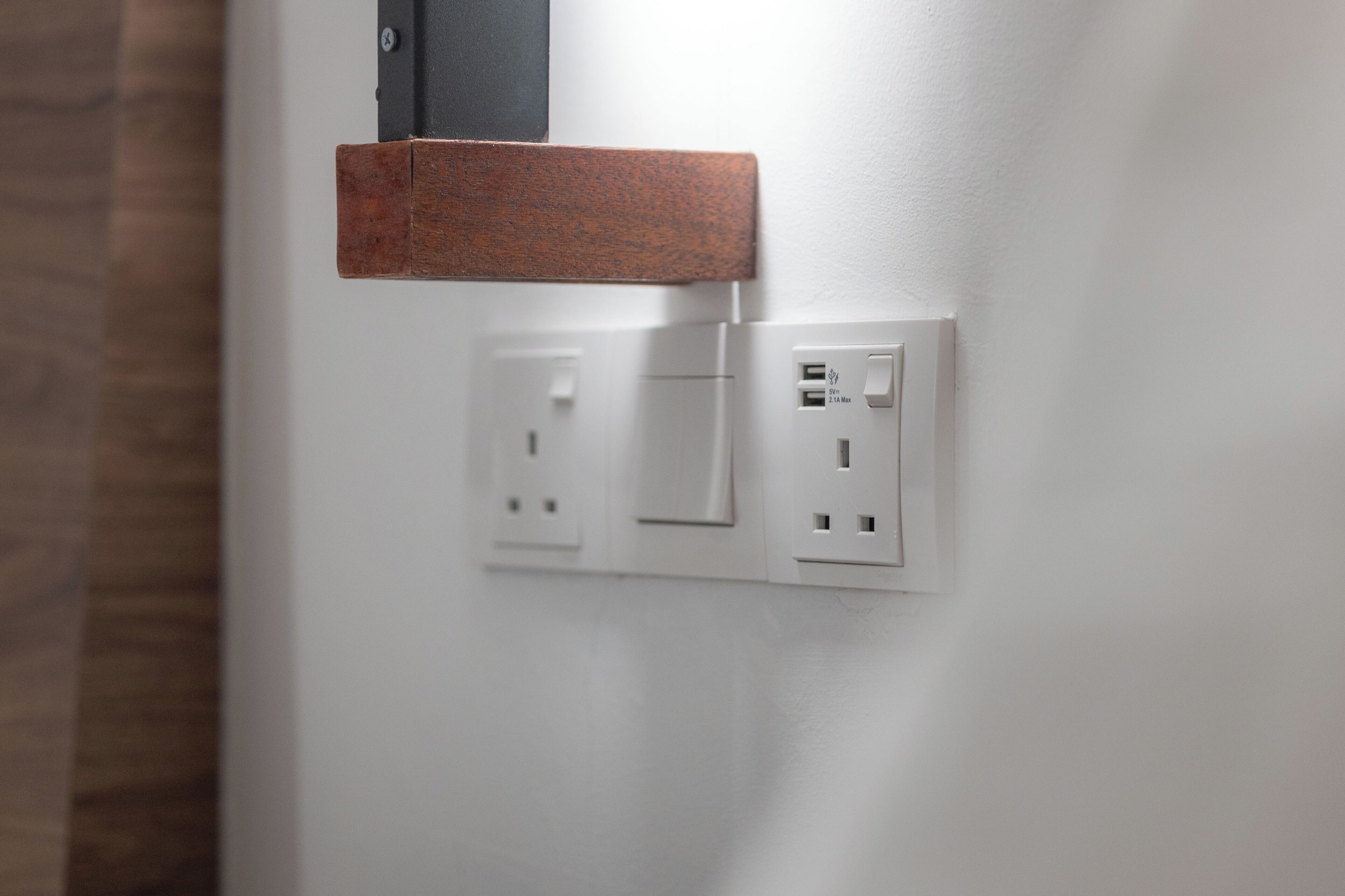 Una pared con dos enchufes y un interruptor, y un estante de madera encima.