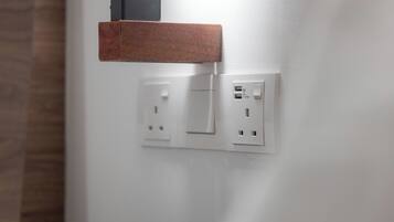 Una pared con dos enchufes y un interruptor, y un estante de madera encima.
