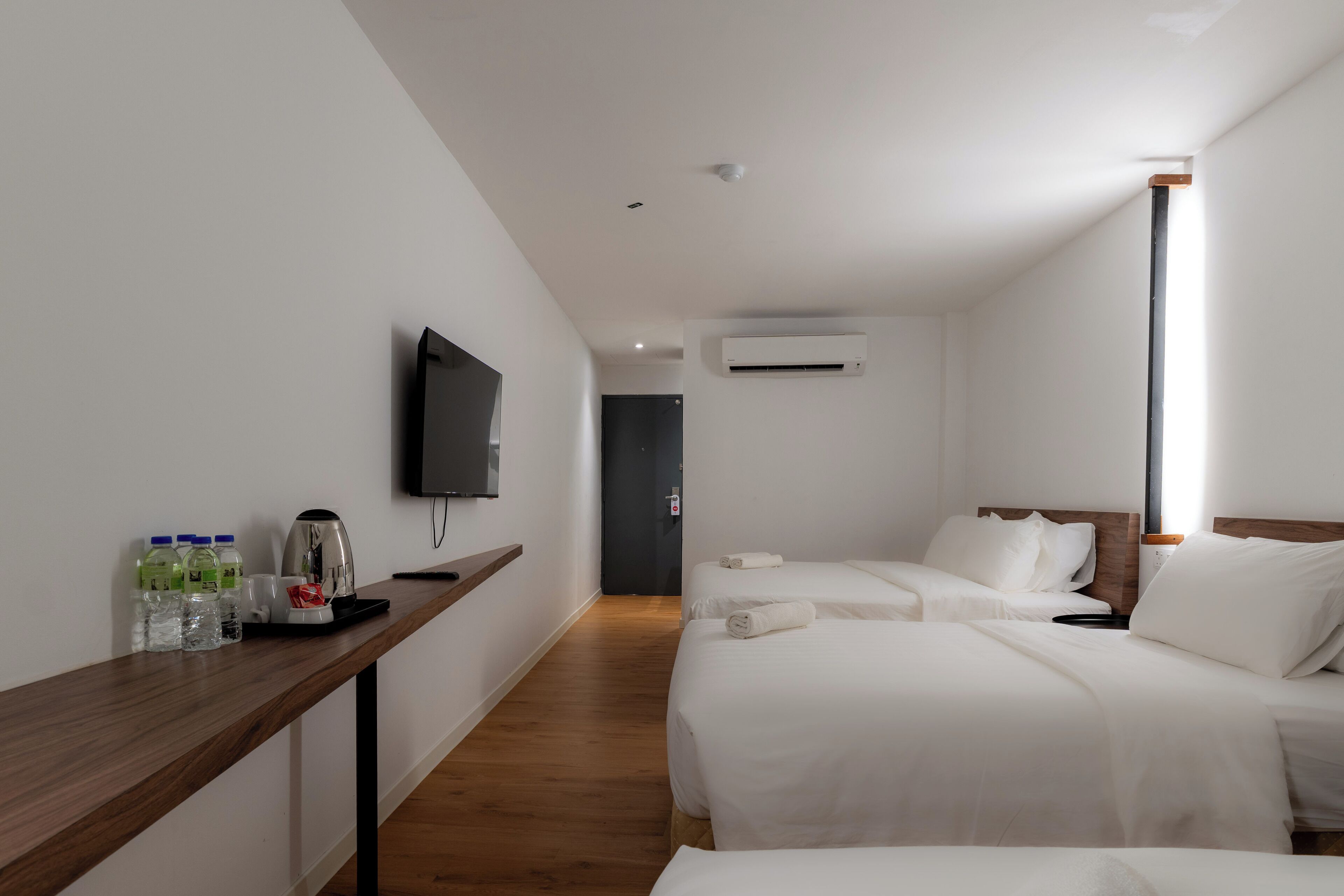 Habitación de hotel con dos camas, un televisor montado en la pared, una cafetera y un dispensador de agua en la mesita de noche.
