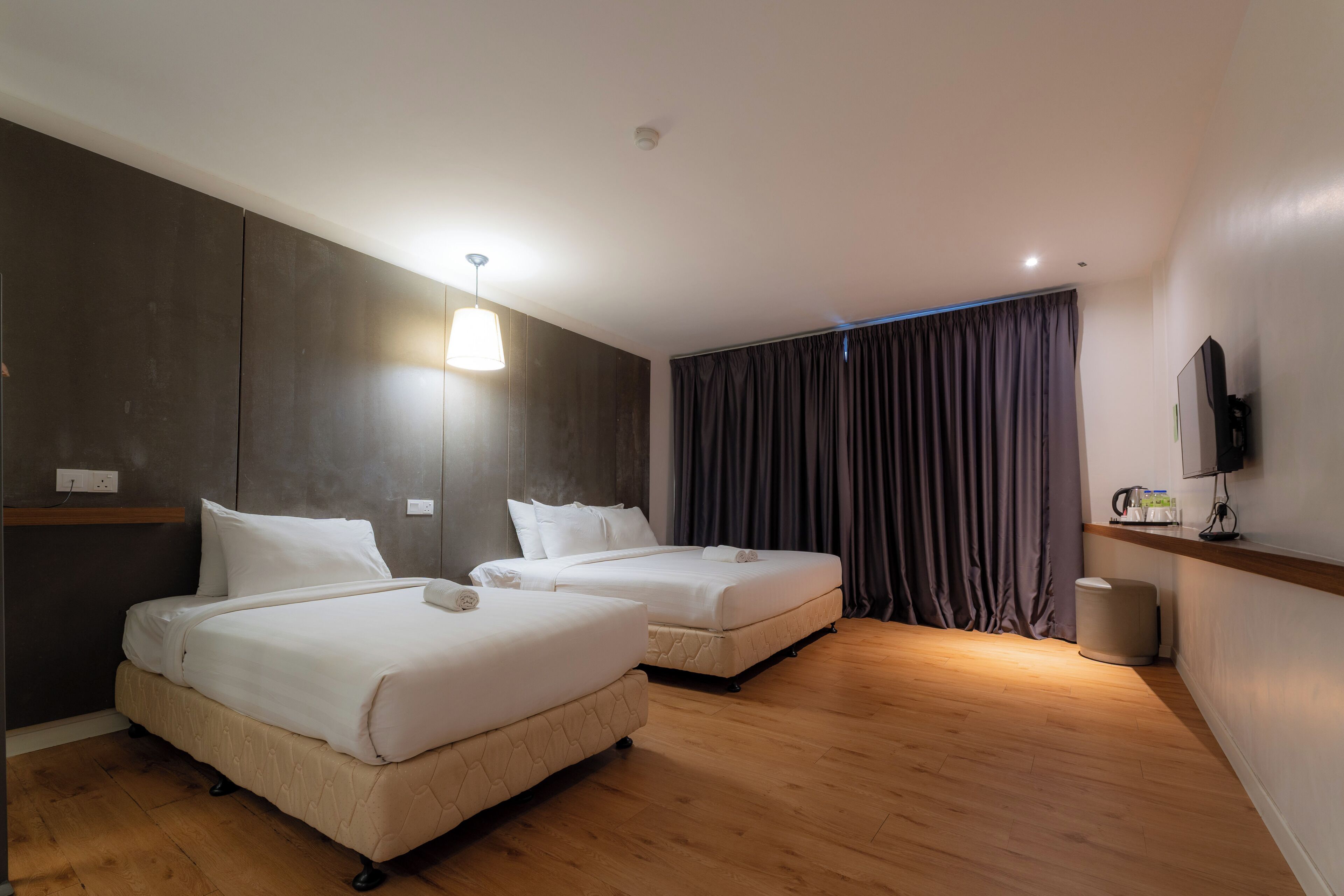 Habitación de hotel con dos camas, piso de madera, televisión de pantalla plana y una mesita de noche con lámpara.