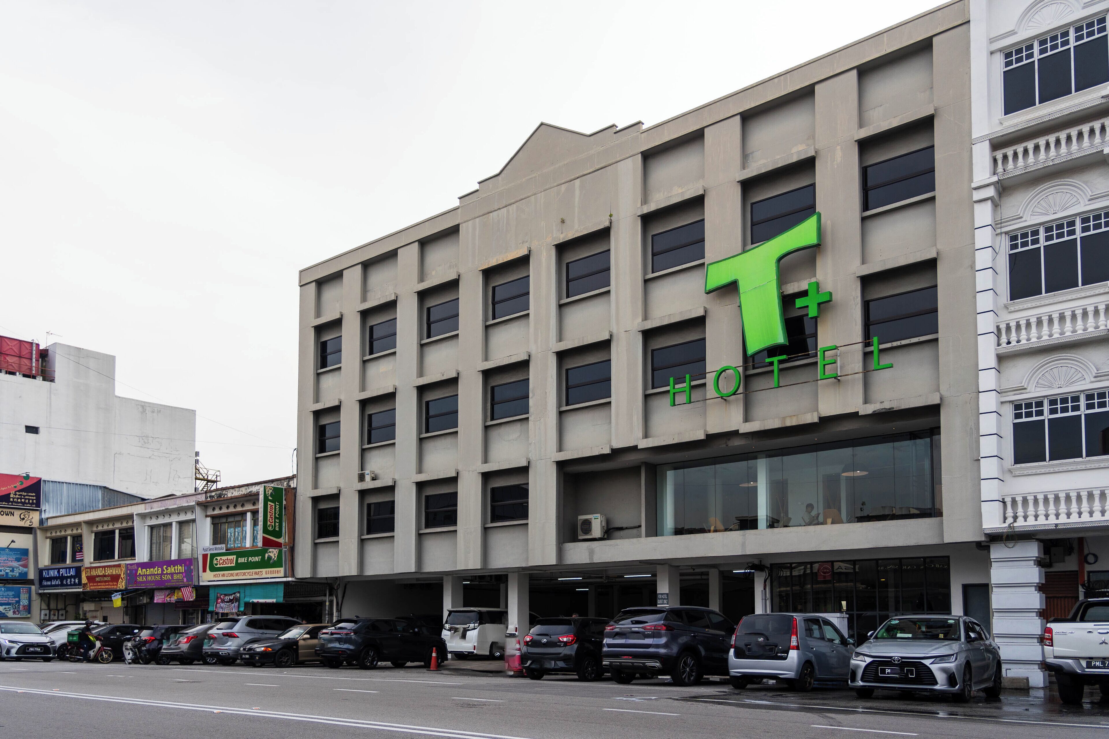 A hotel with a prominent green 'T' sign, multiple floors, and a parking lot with various vehicles.