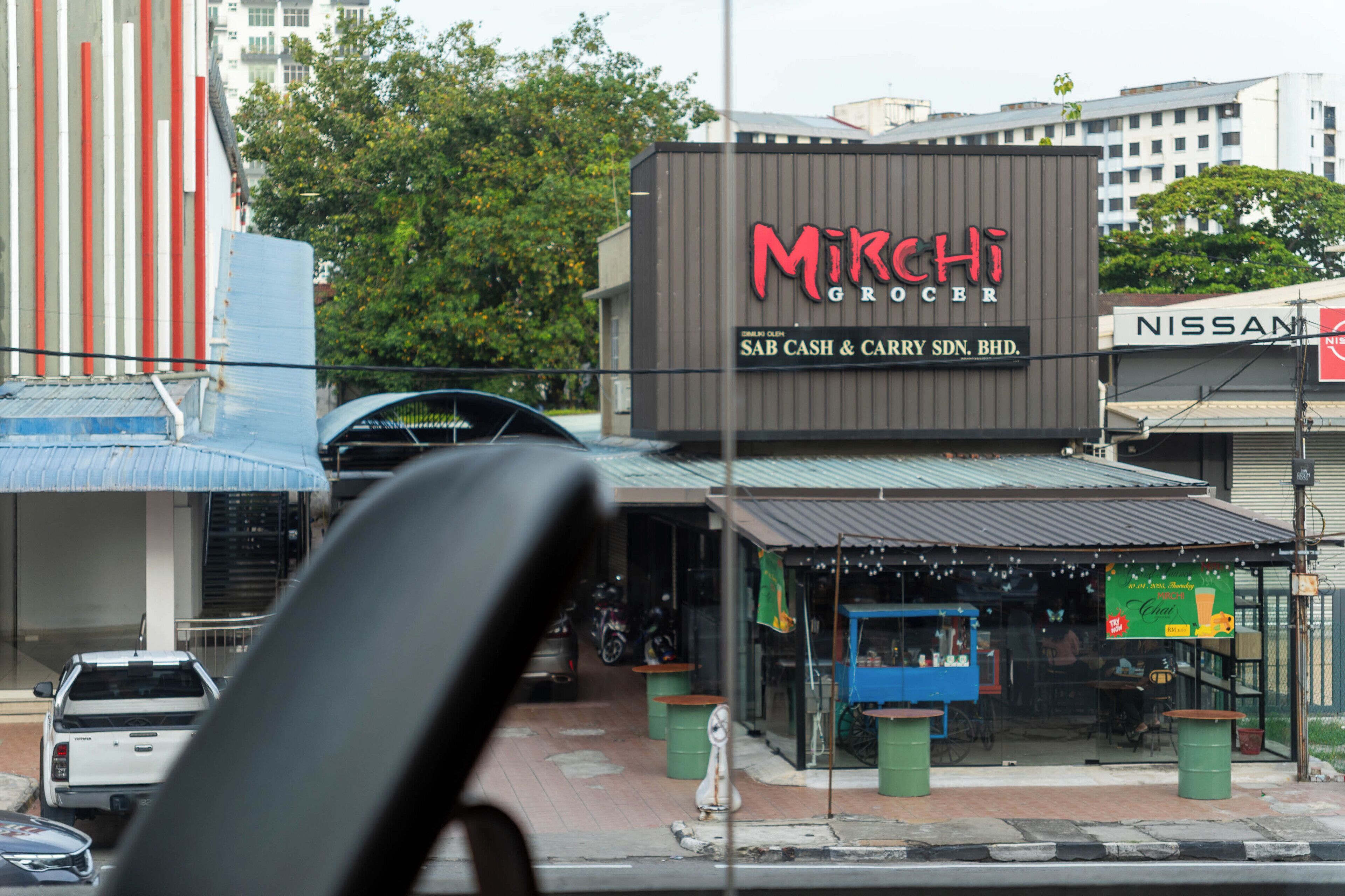 Une épicerie nommée Mirchi, reconnaissable à son enseigne, à un chariot bleu et à une voiture garée devant.
