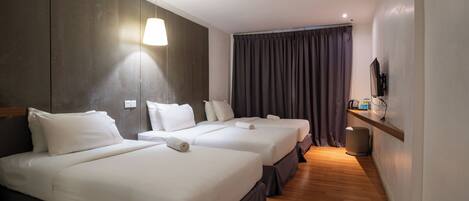 Habitación de hotel con tres camas, un televisor, estante con artículos de aseo y suelo de madera.