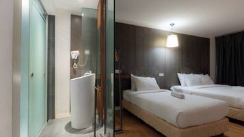 A hotel room with two beds, a glass shower enclosure, a hairdryer, and a hanging light fixture.