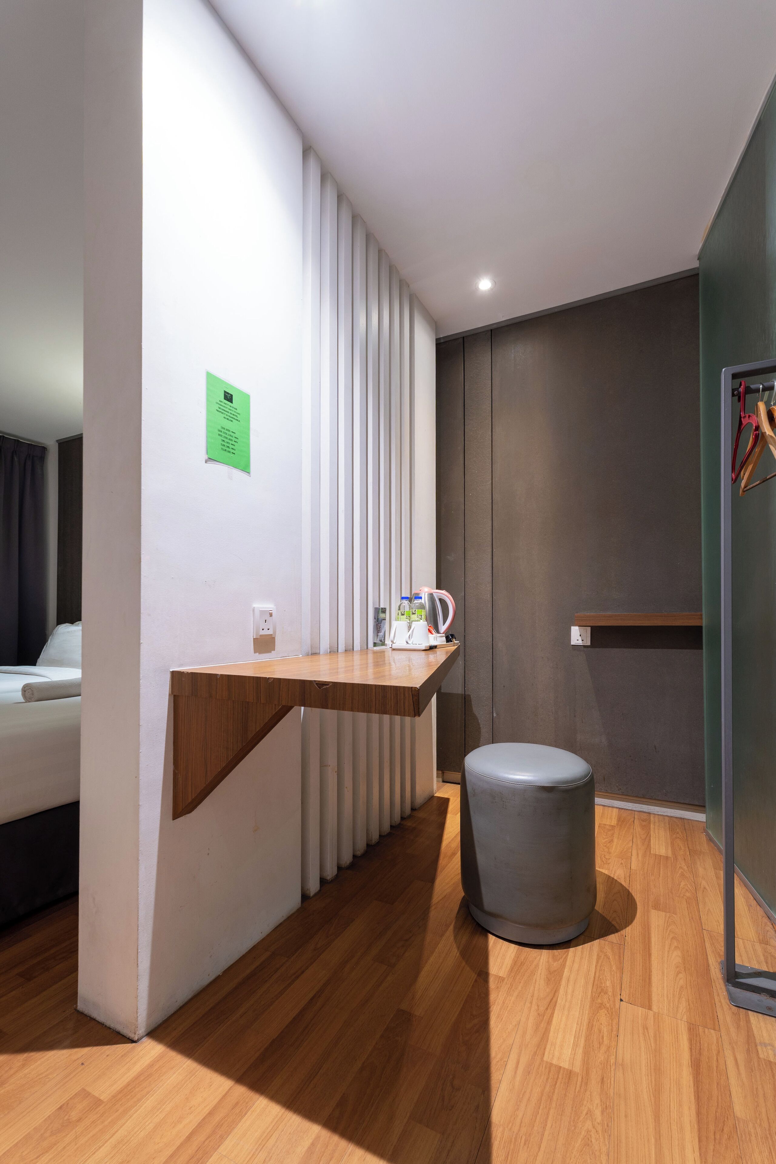 A modern hotel room with a wooden desk, a grey trash bin, a radiator, and a green sign on the wall.