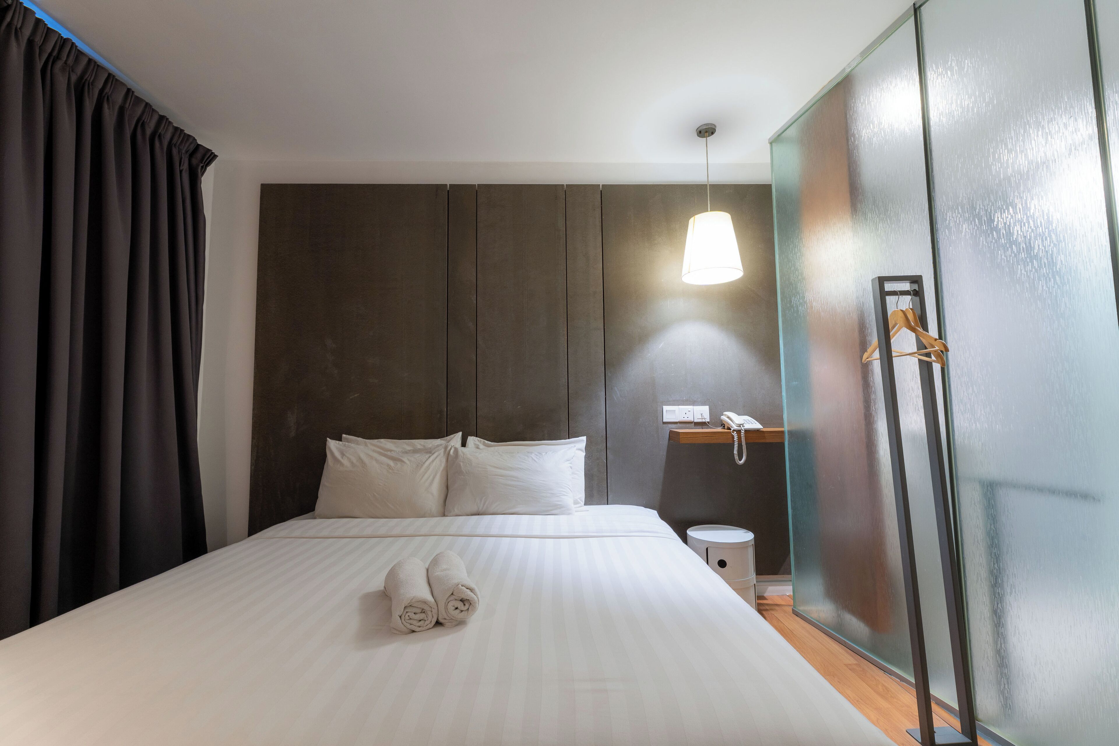 Habitació d'hotel amb un llit gran, una tauleta de nit, una làmpada penjant i un armari.