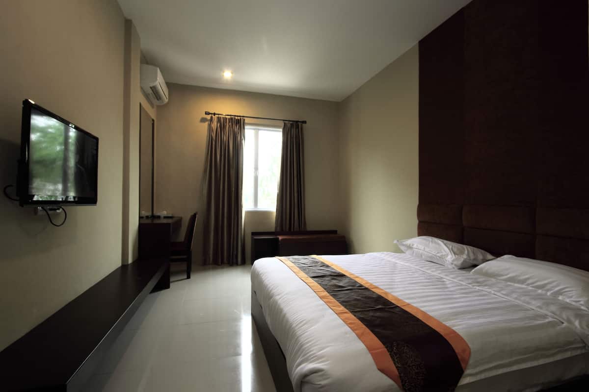 A hotel room with a bed, a desk, a chair, a television, and a window with curtains.