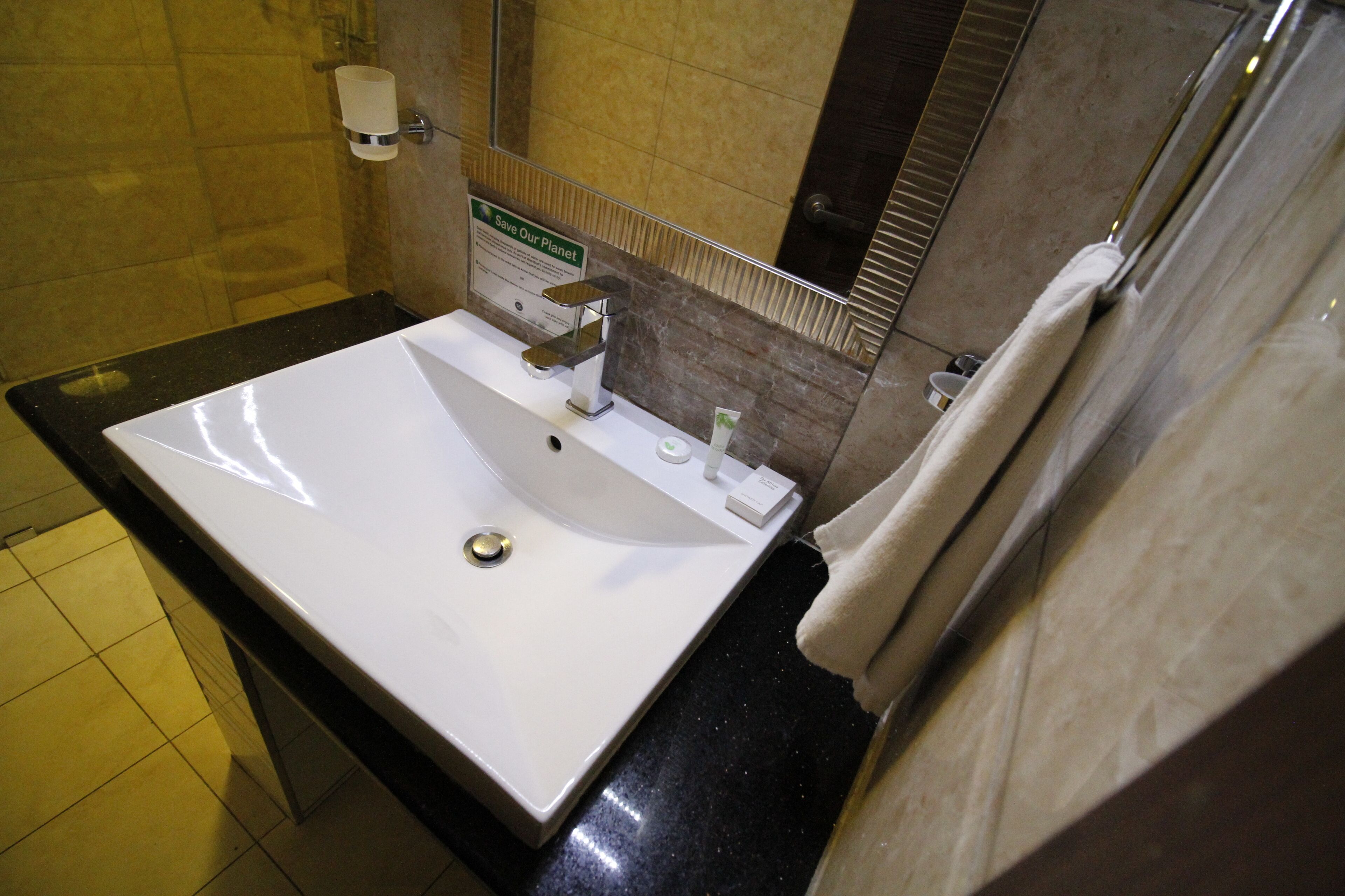 A bathroom with a white sink, a towel hanging on the wall, and a sign promoting environmental conservation.