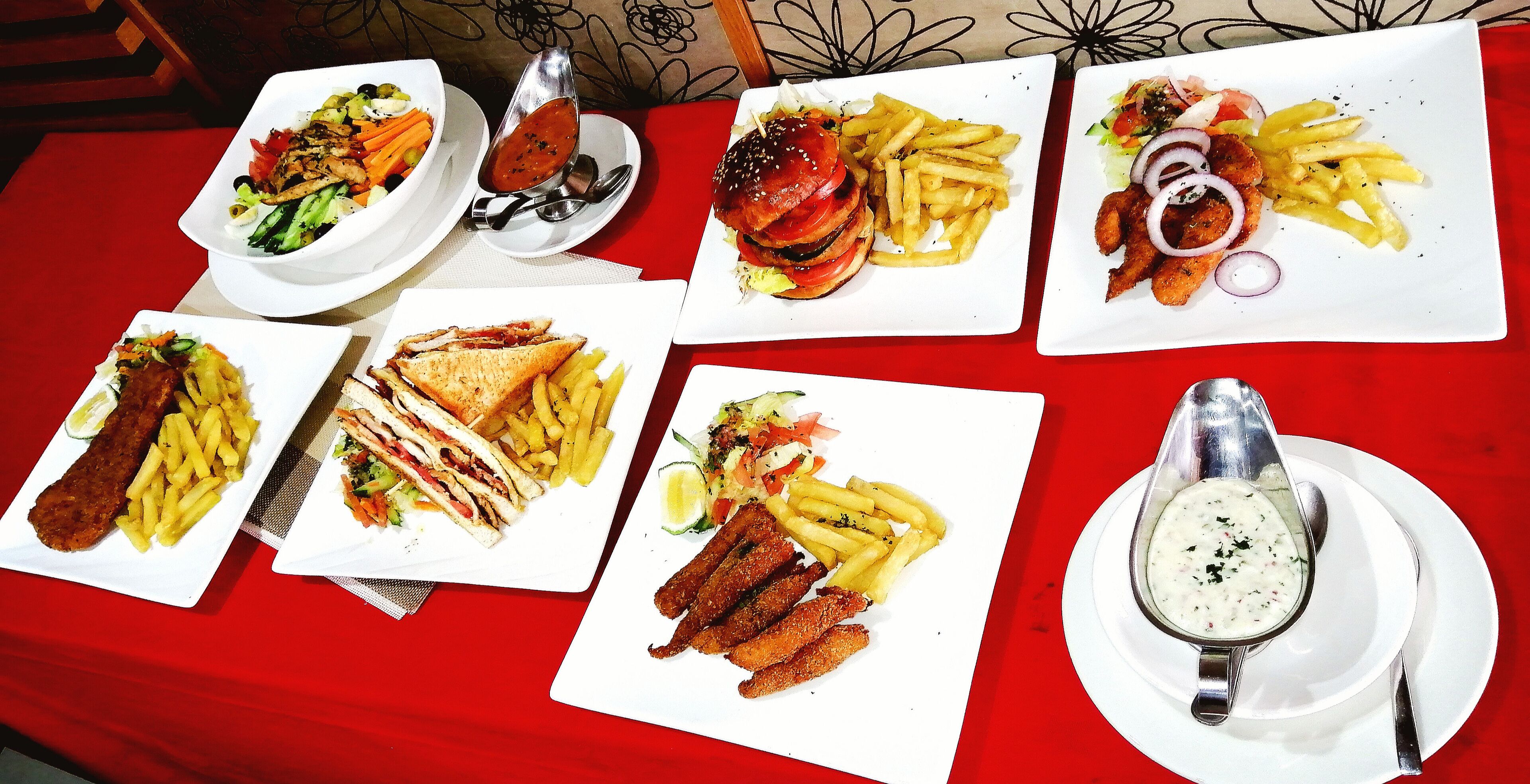 Una mesa con varios platos, incluyendo hamburguesas, papas fritas y sándwiches.