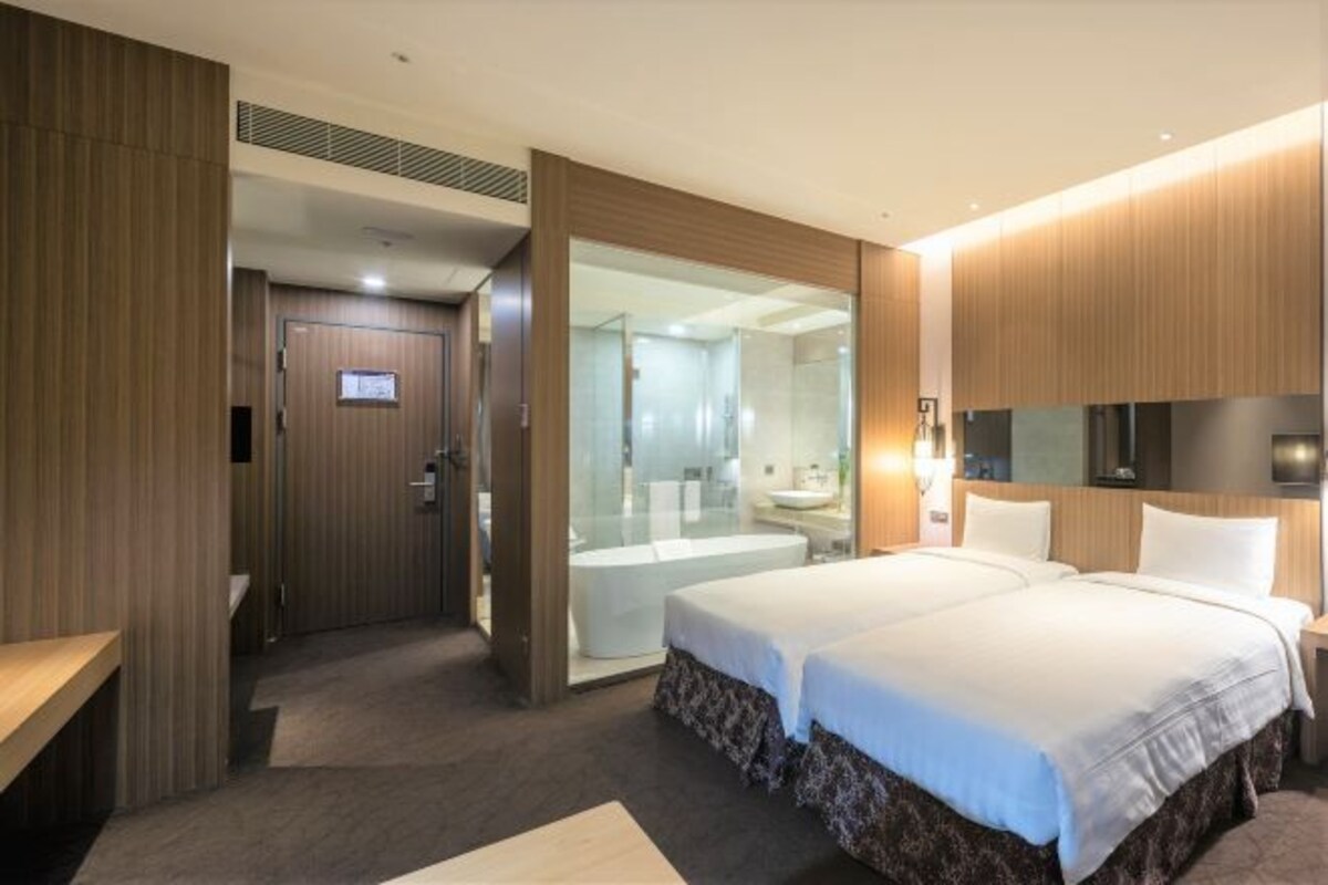 A hotel room with a bed, a bathroom, a desk, and a sliding door to a shower area.