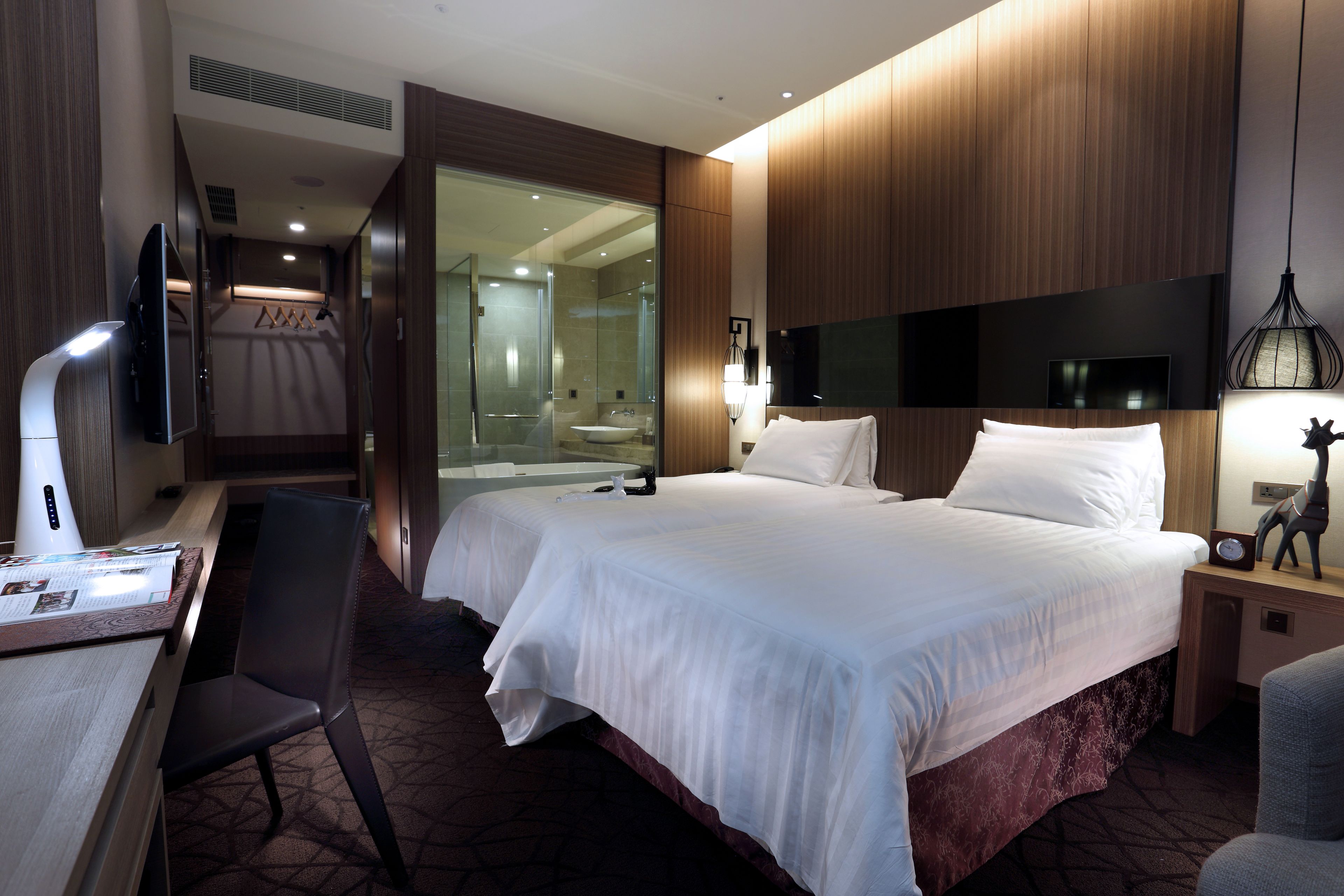 Habitación de hotel con una cama grande, un escritorio, una silla, un televisor y un baño visible a través de una puerta de vidrio.