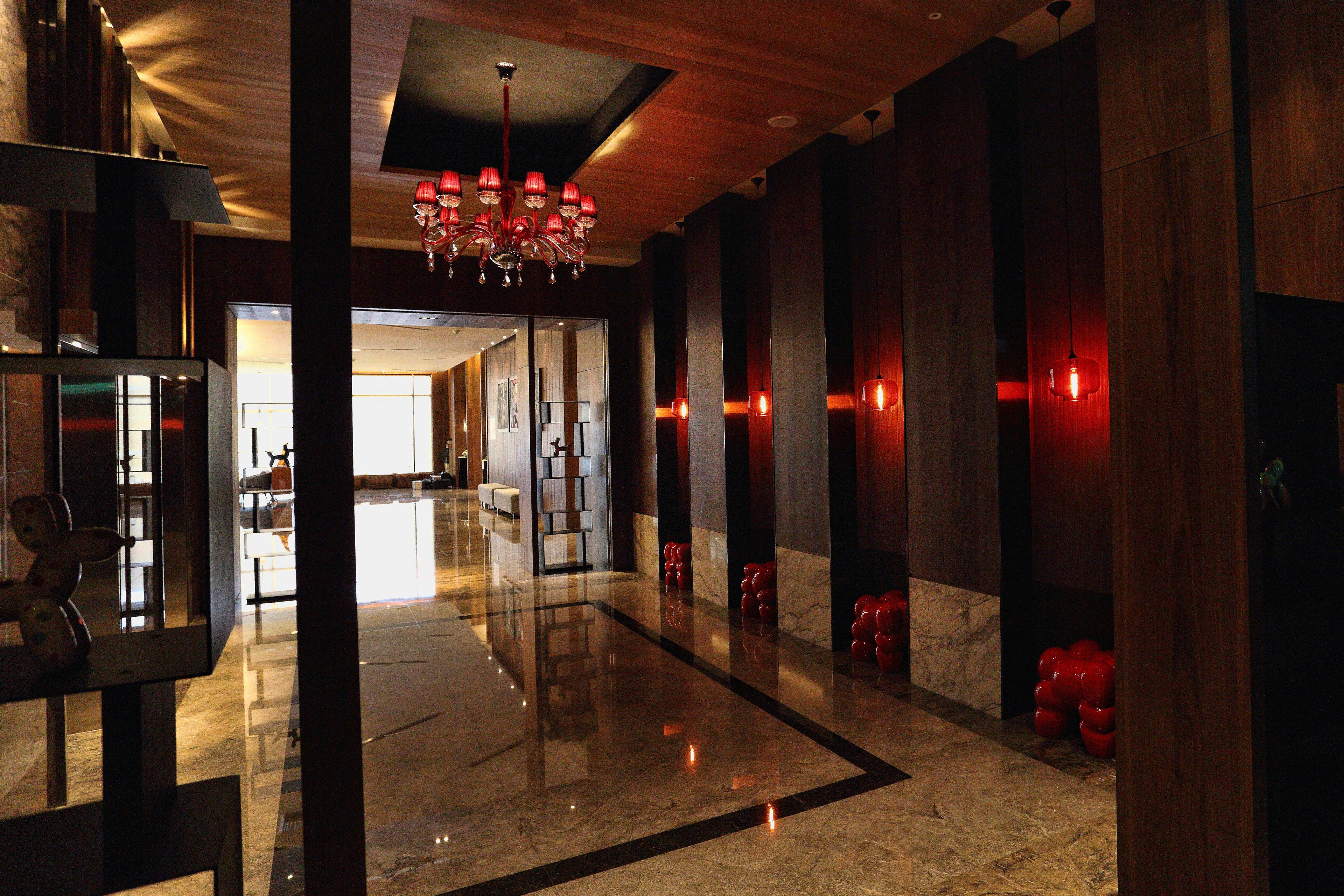 Un moderno vestíbulo de hotel con piso de mármol, una araña y decoraciones esféricas rojas.