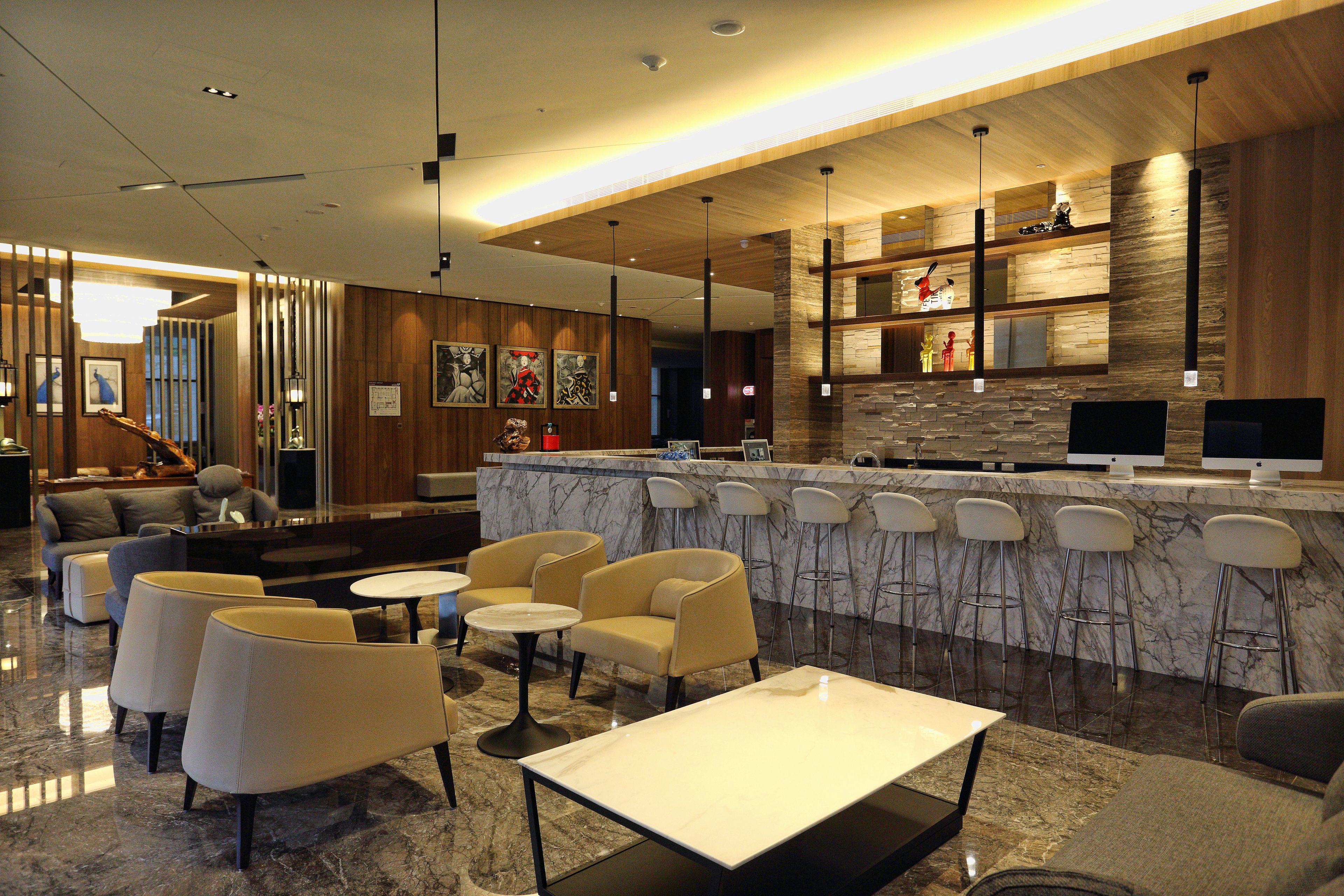 A modern lobby with a marble reception desk, bar stools, sofas, and a seating area with tables.